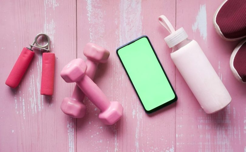 Smart phone with sports equipment on wooden floor.